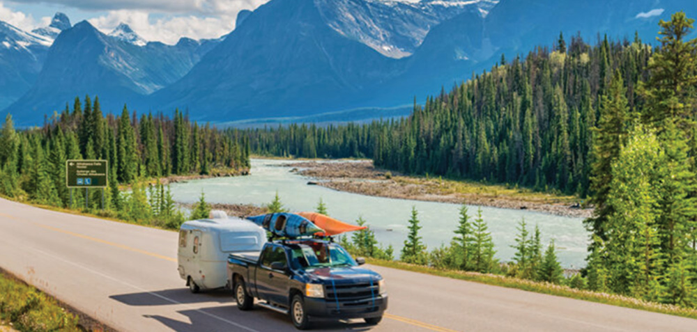 truck driving with a trailer in front of a lake and river