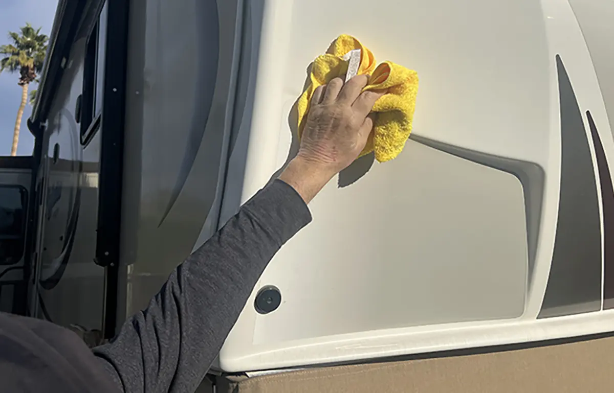 Landscape close-up photo view of a man's arm/hand wiping down the side of an RV with a yellow rag towel