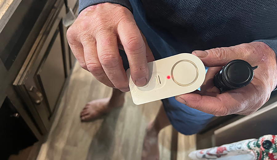 Landscape close-up photo view of a man's fingers holding a Govee H5054 water alarm sensor product model in his hands inside a RV kitchen setting area