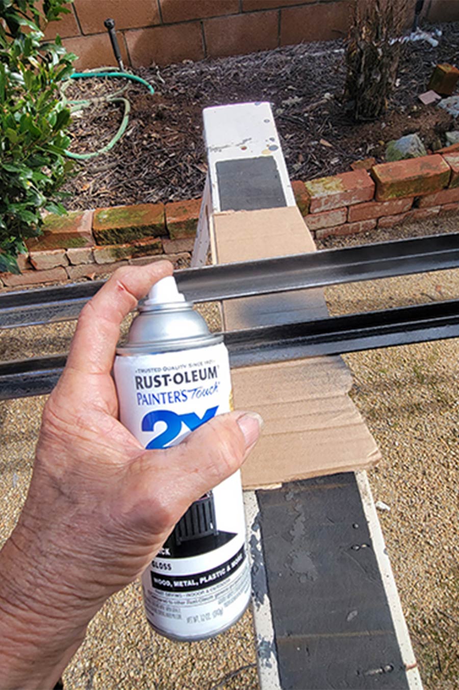 hand holding up a can of primer/paint to spray onto the angle iron