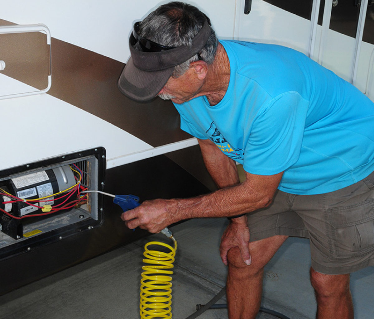 Furnace model being inspected and service by man in blue shirt, brown shorts, and brown visor. 