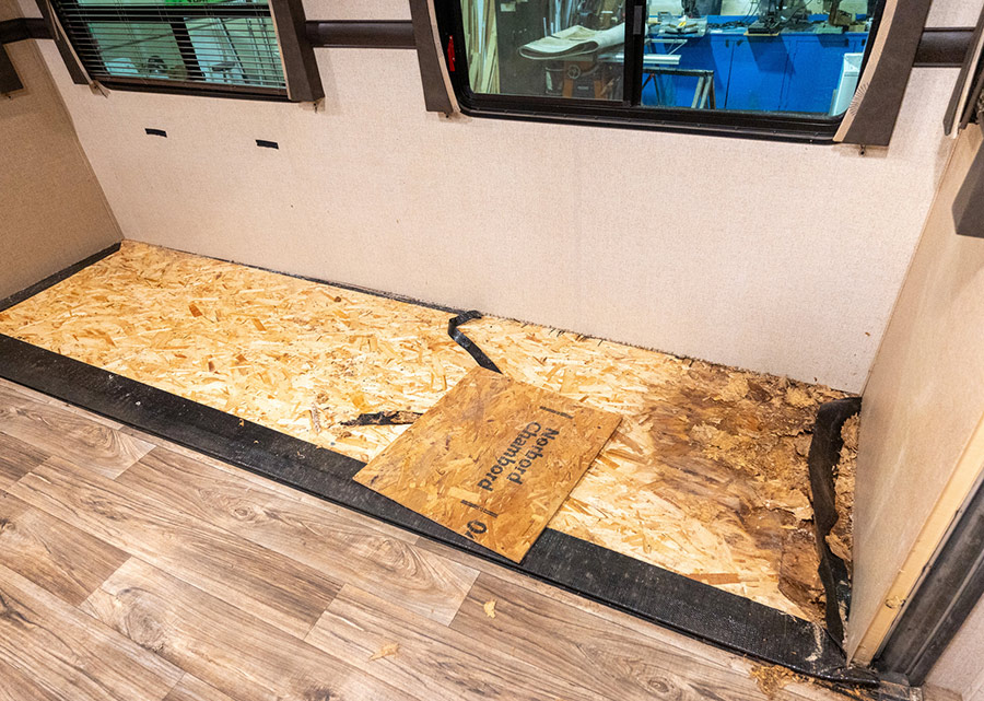 Landscape close-up photo view of a wooden floor board of a small RV interior area being covered with plywood, providing a sturdy and durable surface for the interior