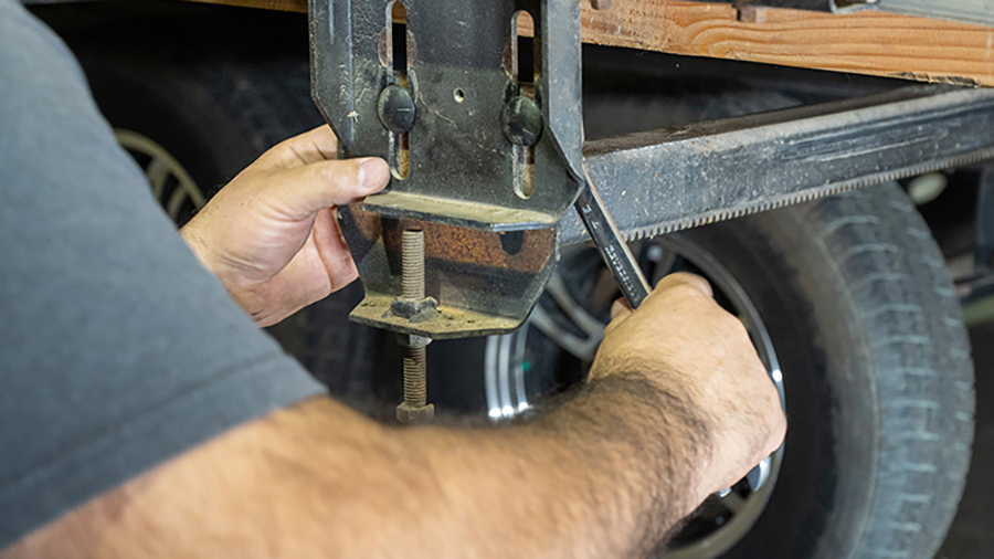 Landscape close-up photo view of a man's arms/hands using a wrench to adjust a particular RV sub-floor replacement area, which was installed by 10-foot-long 4x4s under the slide so it can be lifted by a forklift; Once the weight of the slide is on the forks, it’s unbolted from the two rams and carefully pulled out of the trailer.