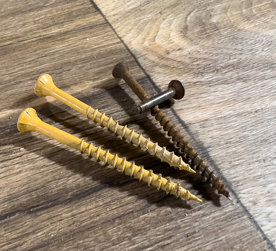 Portrait close-up photograph view of three big wooden screws displayed on a table; two in yellow and one in dark brown with a tinier little dark brown metal screw resting on top of the bigger dark brown wooden screw