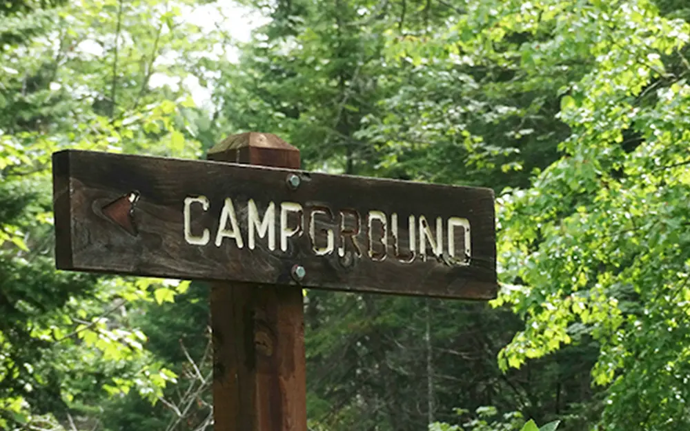 a worn wooden sign engraved with an arrow and the word campground in all caps