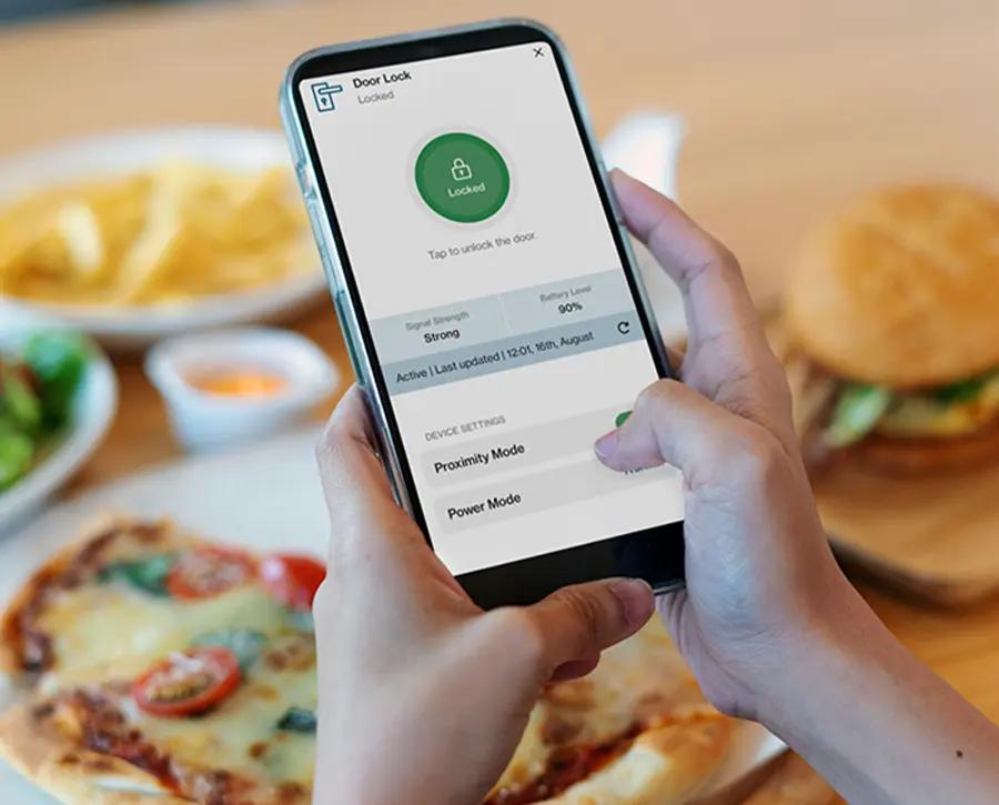 a hand near a diner table holds a smartphone showing a security app interface