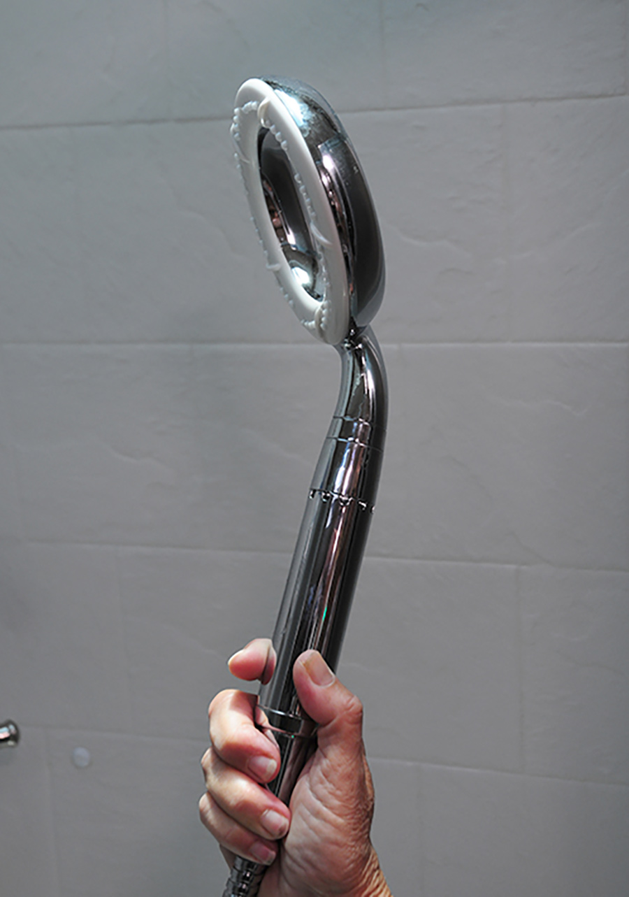 Close-up portrait photograph view of a hand holding the Ecocamel’s Orbit showerhead at an angle in the air