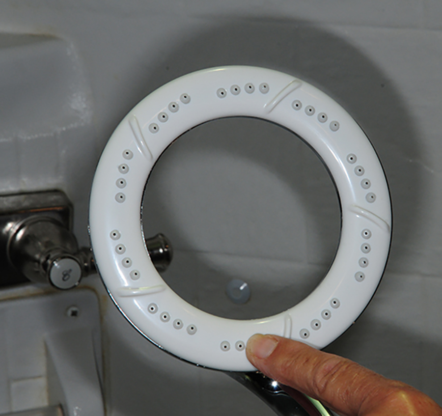 Close-up portrait photograph view of a finger pointing inside the Ecocamel’s Orbit showerhead inner rim at an angle in the air; Unique design of Orbit Soft Water handle allows for a comfortable water stream pattern that provides good body coverage. Orbit Soft Water is a little heavier, but overall length and weight presents no issues when holding over your body. Rubber nozzles in the ring can be cleaned by simply swiping with a thumb. The soft water feature keeps the nozzles clear of calcium, as we discovered after years of full-time use.