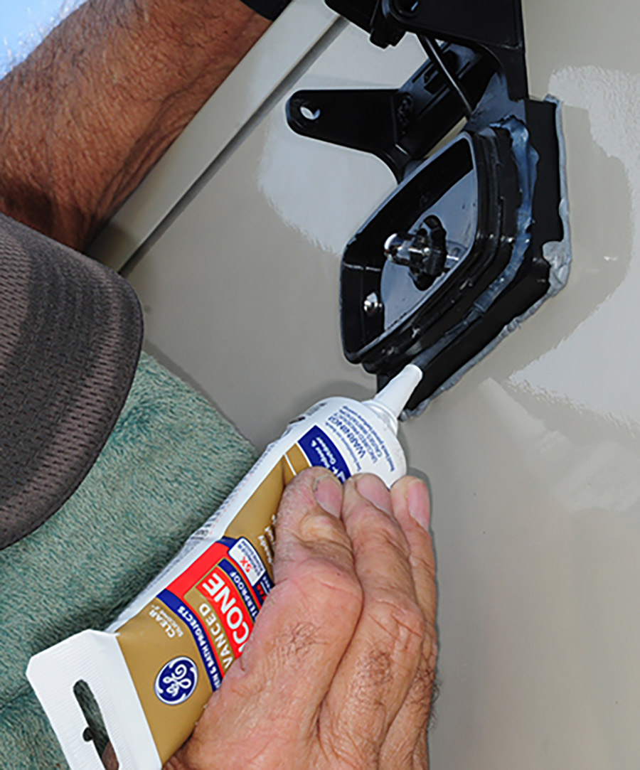 Portrait photograph close-up view of Bill Gehr's hands using a shot of silicone sealant to apply in the gap between the clearance light base and the bracket