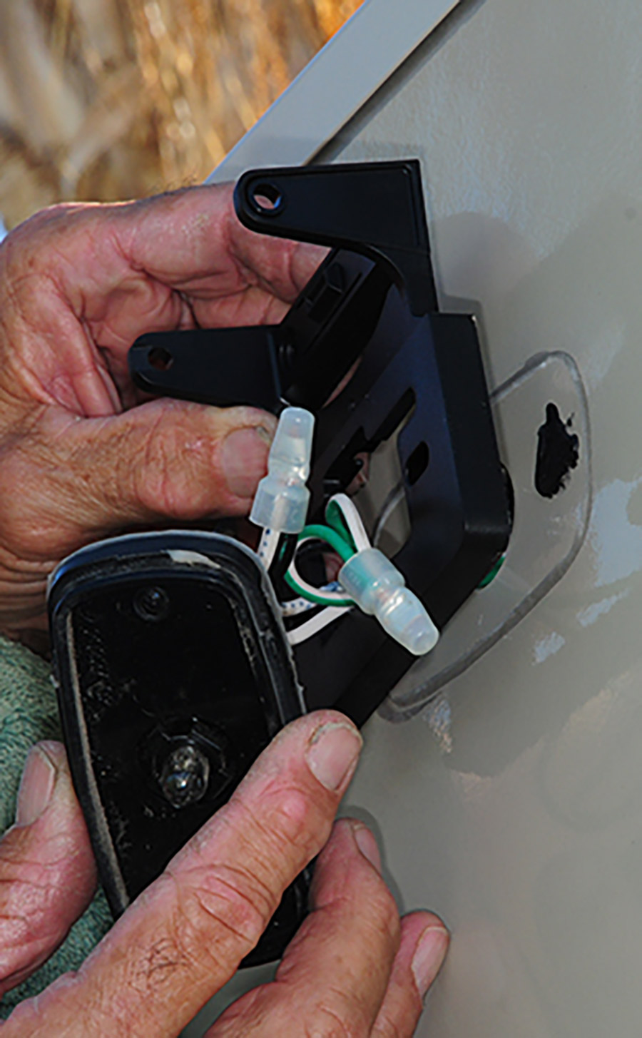 Portrait photograph close-up view of Bill Gehr's hands adjusting the vueSMART bracket as it was first test-fit to make sure it lines up on the back surface area of a RV trailer; Next, the wires were pulled through the bracket.