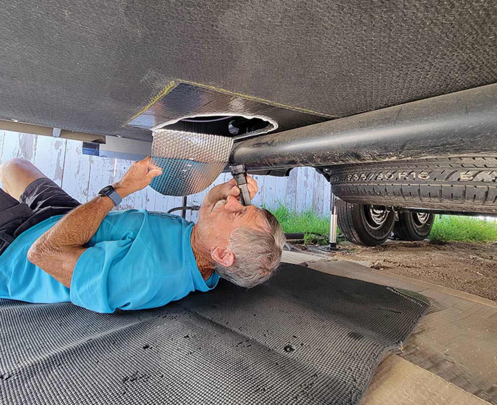 man using a flashlight to inspect the bottom of an RV