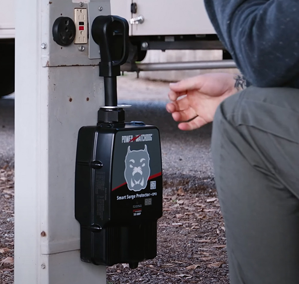 cropped view of a person kneeling in front of a Power Watchdog Smart Surge Protector plugged in to an outdoor power source