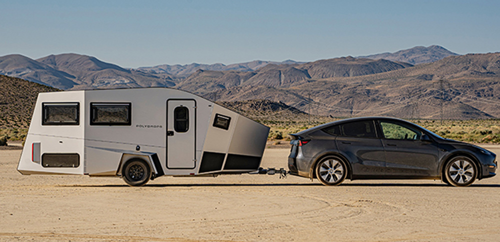 side view of Polydrops new P21 trailer hitched to a Tesla parked on a flat desert plain
