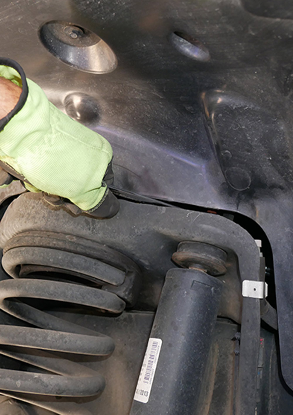a flat wrench is maneuvered between the plastic shroud in the wheel well to remove the bolt on the threaded rod on a front shock